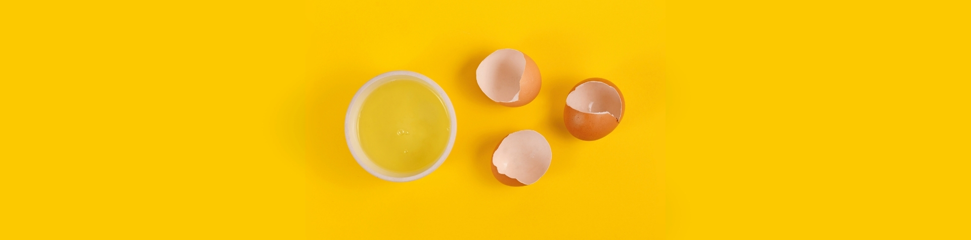 Huevos rotos y un cuenco de clara líquida pasteurizada sobre fondo amarillo